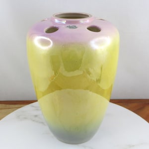 Puede incluir: Un jarrón de cerámica iridiscente amarillo y rosa con cuerpo redondo y parte superior acampanada. El jarrón tiene seis agujeros alrededor del borde superior.