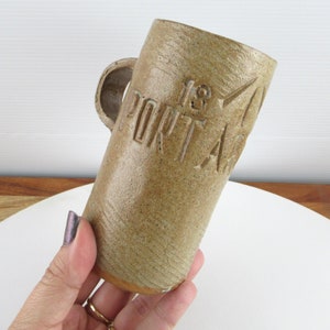 Puede incluir: Una taza de cerámica marrón con asa y el texto "18 PORT AC" en relieve en el lateral.