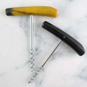 May include: Two T-handle corkscrews with silver-coloured metal spirals. One corkscrew features a smooth, mustard-yellow handle with dark brown accents at the ends, while the other has a solid, polished black handle with a small metal pin detail.