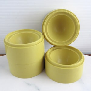 May include: Three cylindrical containers in a matte chartreuse yellow finish. One container is stacked on top of another, while the third sits separately to the right. Each piece features a deep, rounded interior basin and a smooth exterior surface.