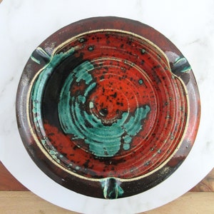 May include: A ceramic ashtray with a brown rim and a swirling pattern of red, orange, and green glaze.