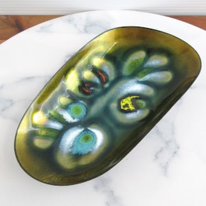 May include: An oval-shaped metal dish featuring a glossy enamel finish in shades of olive green, deep forest green, and gold. The surface displays a swirling, abstract pattern with accents of bright turquoise, yellow, and a small touch of orange.