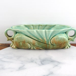 May include: A green and brown ceramic planter with two handles. The planter has a wavy design and a scalloped edge.