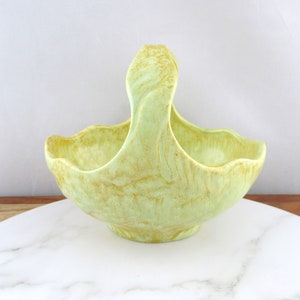 May include: A green ceramic basket with a handle. The basket has a marbled glaze with a yellow and green pattern.