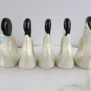 Puede incluir: Cinco anillos de servilleta de cer&aacute;mica blanca con forma de mujeres con cabello negro y detalles coloridos. Los anillos est&aacute;n dispuestos en una fila sobre una superficie blanca.
