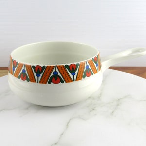 May include: White ceramic serving dish with a handle. The dish has a colourful geometric pattern around the rim in shades of orange, blue, green, and red.