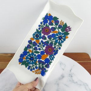 May include: A white rectangular serving tray with a floral design. The flowers are blue, purple, orange, and green. The tray has a scalloped edge.
