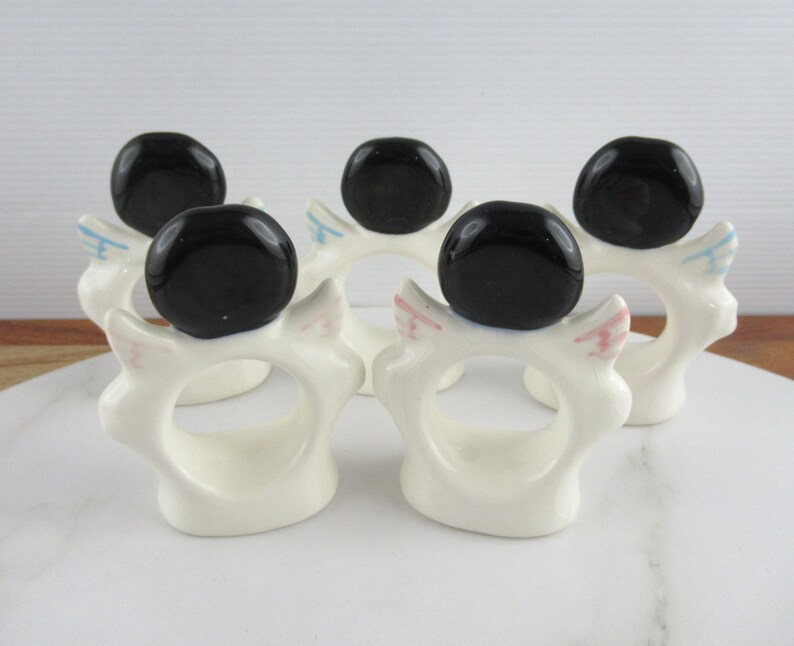 Puede incluir: Conjunto de cinco anillos de servilleta de cer&aacute;mica blanca con tapas de cer&aacute;mica negra. Cada anillo tiene un dise&ntilde;o rosa y azul en el lateral.
