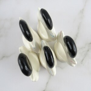 Puede incluir: Conjunto de cinco anillos de servilleta de cer&aacute;mica blanca en forma de cisne con detalles negros. Cada anillo presenta un cisne con cabeza y cuello negros y cuerpo blanco. Los anillos son perfectos para a&ntilde;adir un toque de elegancia a cualquier mesa.