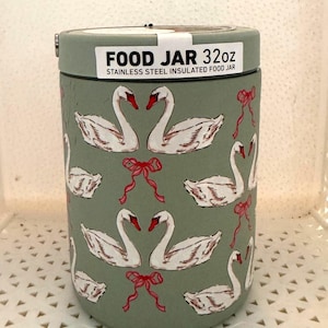 May include: A sage green stainless steel insulated food jar with a 32oz capacity. The exterior features a repeating pattern of white swans with red beaks and small red bows. A white label on the lid reads FOOD JAR 32oz STAINLESS STEEL INSULATED FOOD JAR.