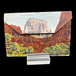 May include: Vintage postcard featuring a landscape of Zion National Park, with the text "The Great White Throne, Zion National Park." The postcard has a clear, rectangular display stand in front of it.