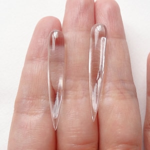 May include: Two clear glass teardrop-shaped earrings with pointed ends.