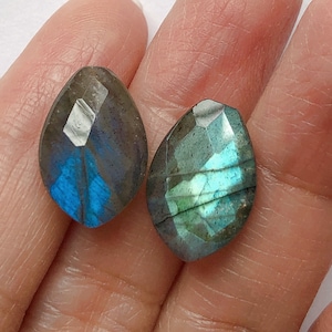 Può includere: Coppia di cabochon di labradorite blu e verde iridescenti, etichettati "Pair A", tenuti in una mano.