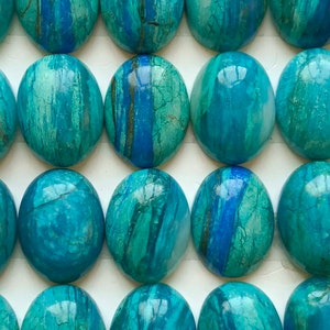Può includere: Un foglio di 18 cabochon ovali in turchese, ognuno misura 12x16 mm. I cabochon sono una miscela di blu e verde con venature bianche. I cabochon sono etichettati "Gruppo A".