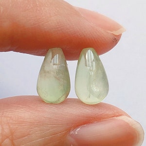 Può includere: Due pietre preziose verdi a forma di goccia, di colore verde chiaro e traslucide.