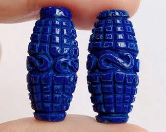 Può includere: Due perline blu in lapislazzuli con intricati disegni intagliati. Le perline sono di forma ovale e hanno una superficie testurizzata.