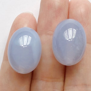 Può includere: Due cabochon ovali in calcedonio blu, ciascuno con una superficie liscia e lucida. Le pietre sono di colore blu chiaro con una leggera traslucenza.