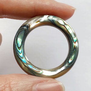May include: A ring made of iridescent abalone shell with a smooth, polished finish. The ring has a round shape and a wide band.