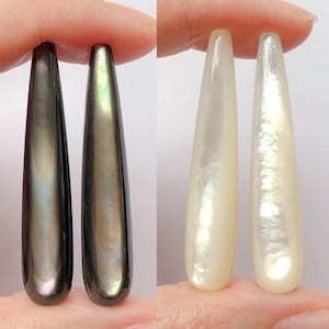 Può includere: Due paia di orecchini lunghi a forma di lacrima, in conchiglia iridescente. Un paio è nero e verde, l'altro è bianco.