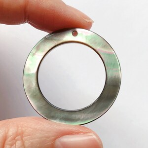 May include: A round, black and green iridescent shell pendant with a hole for stringing. The pendant is about 2 inches in diameter.