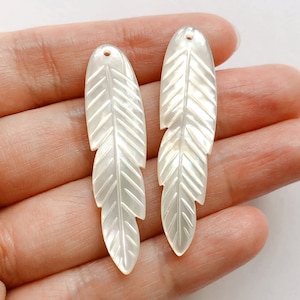 May include: Two white mother of pearl feather shaped pendants with a hole at the top for stringing.