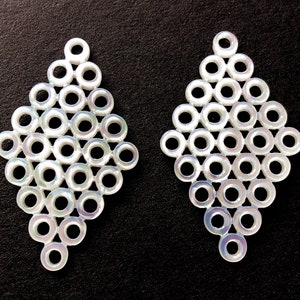 Könnte beinhalten: Ein Paar weiße, rautenförmige Ohrringe aus ineinandergreifenden Kreisen.