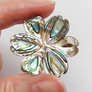May include: An iridescent abalone shell flower with a five-petal design. The flower is a light brown colour with green and blue iridescent accents.