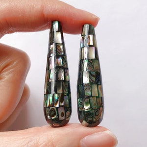 May include: A pair of teardrop-shaped earrings made of black and green abalone shell. The shell is cut into small squares and arranged in a mosaic pattern.