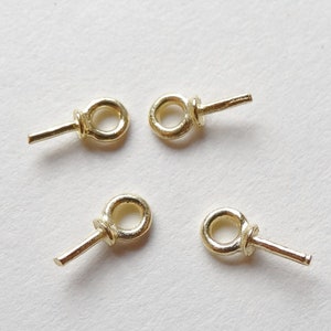 May include: Four small, gold-colored eye pins with a loop and a straight post. The pins are arranged on a white surface, with each pin showing a small loop and a straight post extending from the loop.