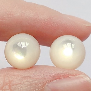 Könnte beinhalten: Zwei weiße runde Perlen, eine in jeder Hand, mit einem leichten irisierenden Schimmer.