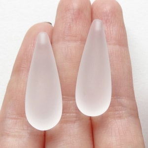 Può includere: Due perline di vetro smerigliato a forma di goccia. Le perline sono traslucide e hanno una finitura liscia e lucida.