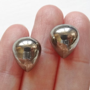 Può includere: Due perline argentate a forma di lacrima con una finitura liscia e lucida.