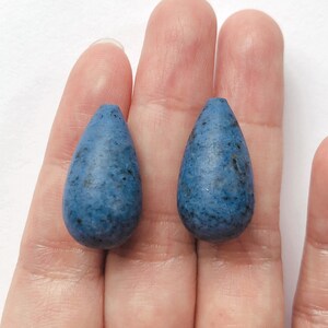 May include: Two teardrop-shaped blue glass beads with a speckled texture.