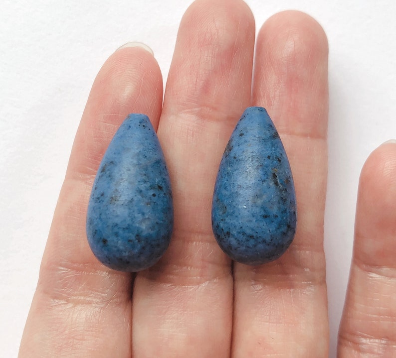 May include: Two teardrop-shaped blue glass beads with a speckled texture.