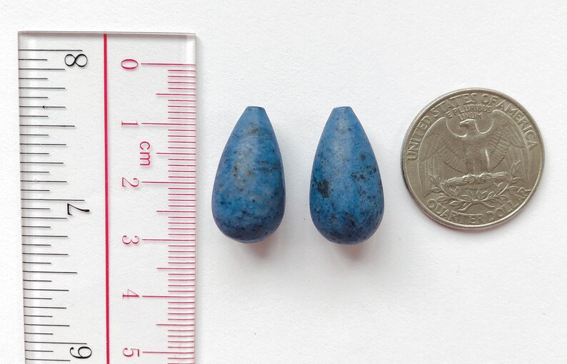May include: Two teardrop-shaped blue beads with a speckled texture, next to a US quarter for size comparison.