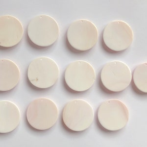 May include: Twelve white round shell pendants with a hole in the center. The pendants are arranged in three rows of four.