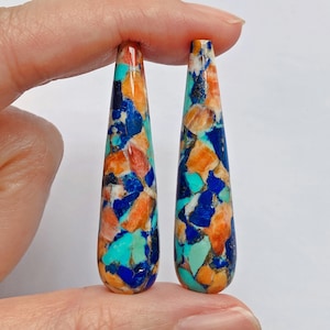 Può includere: Un paio di ciondoli in pietra a forma di goccia con una miscela di colori blu, arancio e turchese. Le pietre sono lucidate e hanno una finitura liscia e lucida.