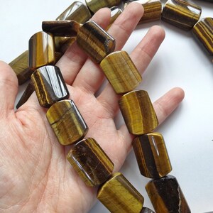 May include: A strand of tiger's eye beads, each bead is a rectangular shape with rounded edges. The beads are a mix of brown, gold, and black colors with a shimmering effect.
