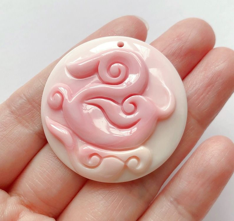 May include: A round, white and pink, carved, decorative pendant with a swirling design.