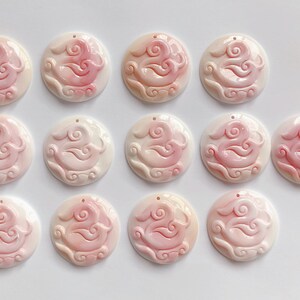 May include: Twelve round, white and pink shell pendants with a carved design of a bird and clouds.