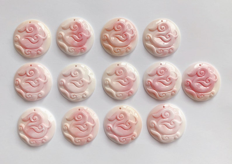 May include: Twelve round, white and pink shell pendants with a carved design of a bird and clouds.