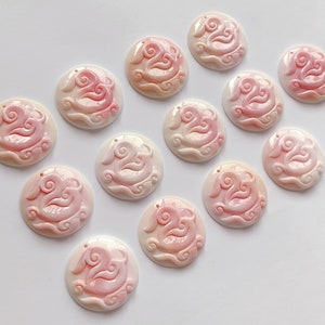May include: A collection of 12 pink and white shell pendants with intricate carvings of clouds and a bird. The pendants are arranged in a circle on a white background.