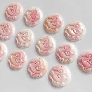 May include: Twelve pink and white shell cabochons with a carved design of a rabbit and clouds. The cabochons are approximately 1 inch in diameter.