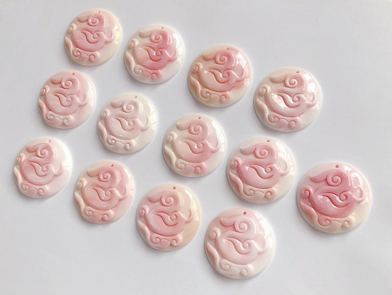 May include: Twelve pink and white shell cabochons with a carved design of a rabbit and clouds. The cabochons are approximately 1 inch in diameter.