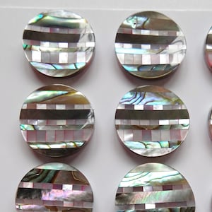 May include: Ten round iridescent abalone shell buttons with a geometric pattern of black, white, and pink squares and stripes.