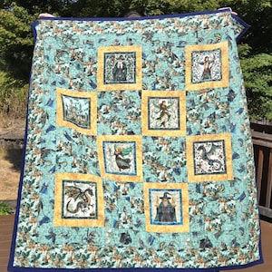 May include: A patchwork quilt featuring a repeating pattern of dragons, wizards, and castles on a light blue background. The quilt includes six square panels framed in gold fabric, each depicting a fantasy character or scene, finished with a dark blue border.
