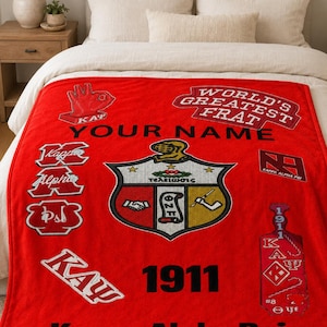 May include: A bright red fleece blanket featuring the Kappa Alpha Psi fraternity crest, the text "WORLD'S GREATEST FRAT," "YOUR NAME," "1911," and "Kappa Alpha Psi." The design includes various fraternity symbols, logos, and Greek lettering.