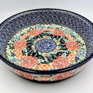 May include: Round ceramic baking dish with two handles. The dish features a floral design with pink roses, blue accents, and a navy blue rim. The interior has a light green background.