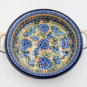 May include: Round ceramic serving dish with two handles. The dish features a blue floral pattern with accents of yellow and orange on a cream background. The rim and handles are blue.