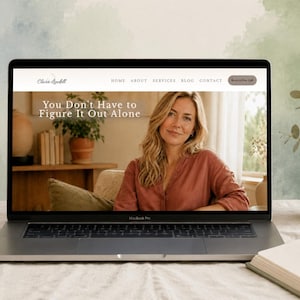 Op de afbeelding: Een laptop toont een website met de tekst "You Don't Have to Figure It Out Alone." Een mok, een plant in een pot en een boek liggen op de tafel. De laptop is open en toont een vrouw in een roestkleurig overhemd.